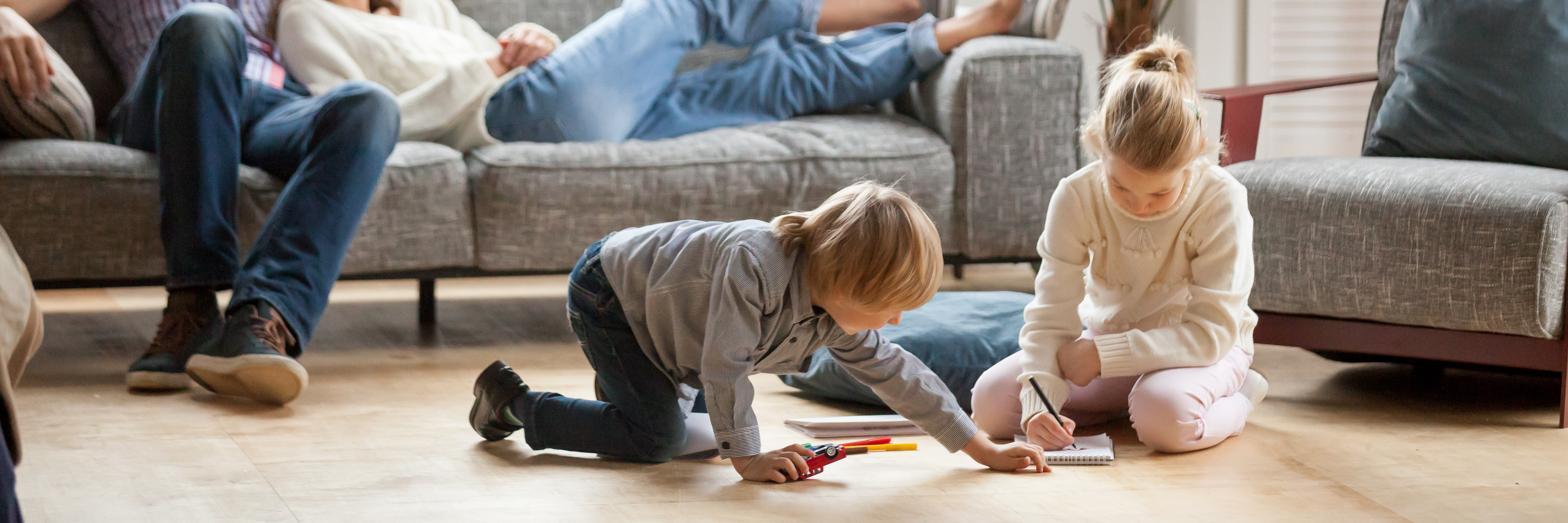 little kids playing on floor of living room with parents on couch